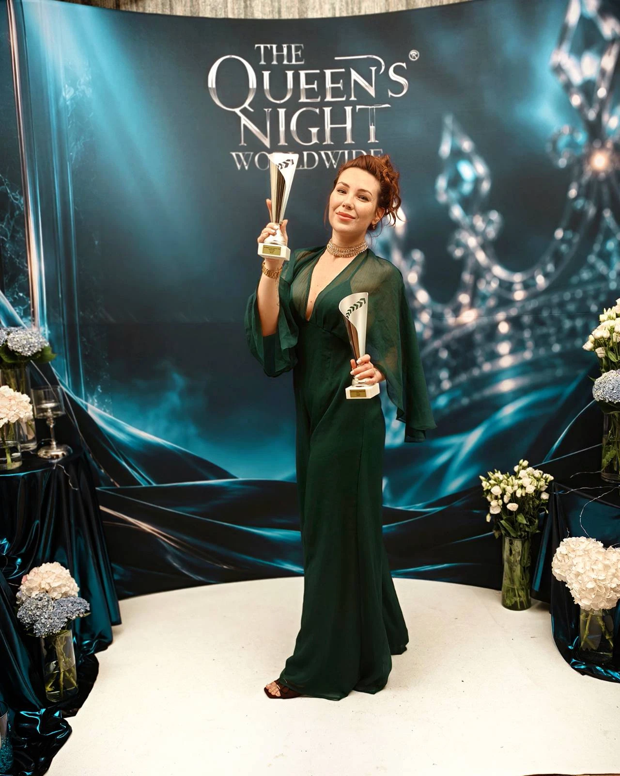 Dorina a The Queen's Night Worldwide plakátja előtt, a két ezüstérmes kupával (2026)